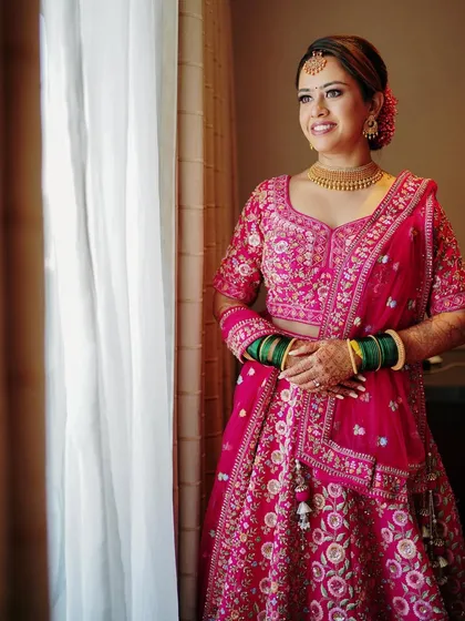 A bride looking out the window, perhaps dreaming of her future. This classic pose, combined with her vibrant pink lehenga, creates a beautiful and hopeful portrait.