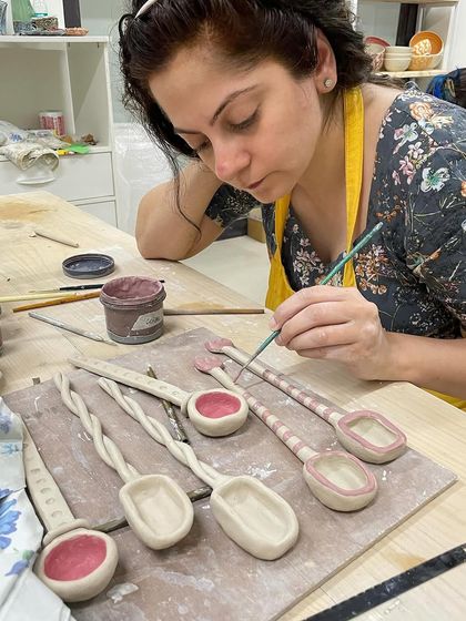 A student meticulously paints details onto a set of hand-built ceramic spoons, turning everyday objects into works of art.