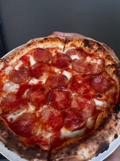 A full view of the Hungarian Salami pizza, held up to show off its perfectly round shape and generous toppings.