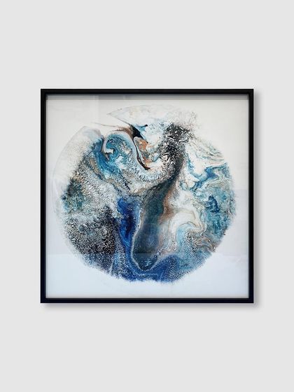 This abstract artwork, reminiscent of a swirling planet, is elegantly contained within a square black metal frame, adding a touch of modern sophistication.