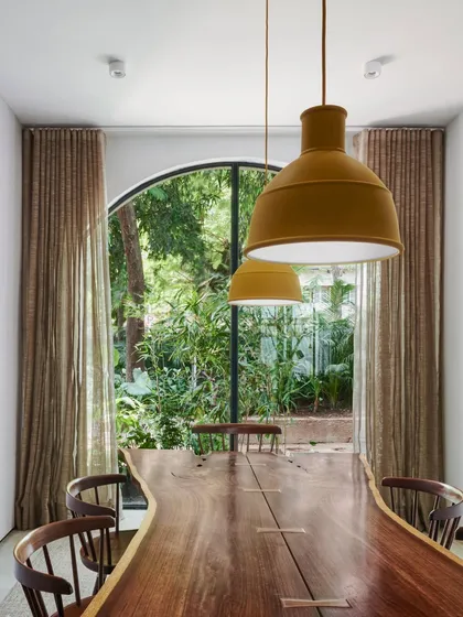 The dining table in our studio, framed by an arched French window that looks out onto lush greenery. This seamless integration of indoor and outdoor living is a principle we apply to our own workspace.