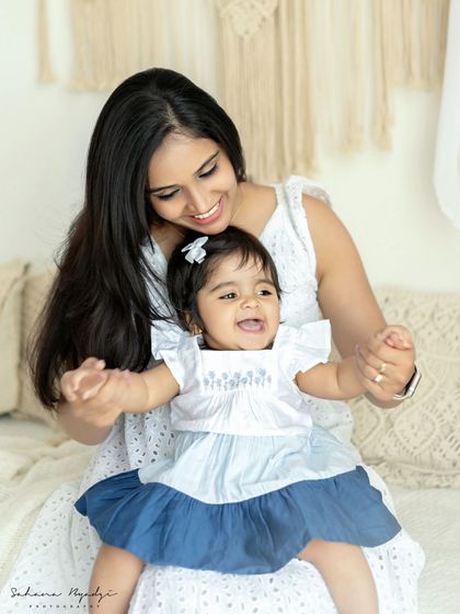 A mother and her happy baby girl, both sharing a beautiful smile. The simple, bright setting keeps the focus on their joyful interaction and connection.
