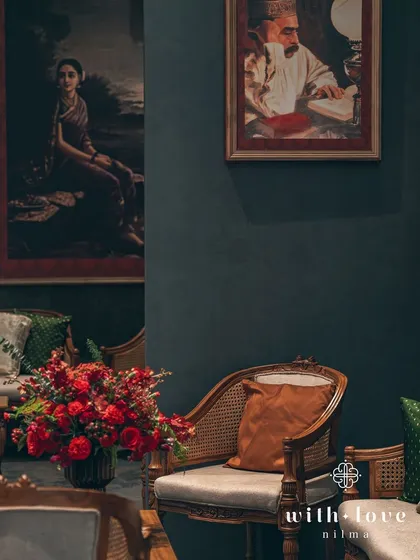 An intimate seating nook with classic cane-back chairs and plush cushions. The space is designed to feel like a cozy corner in a heritage home, surrounded by beautiful art and soft lighting.