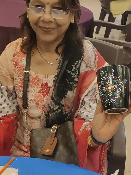 An elegant participant smiles as she displays the colourful dot art mug she created during a group workshop. This highlights how art is an enjoyable activity for people of all ages.