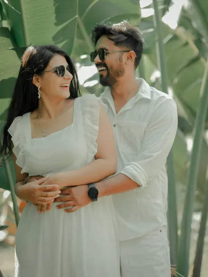 A fun and carefree moment captured against a backdrop of lush tropical leaves. The couple, dressed in matching white, shares a laugh, showcasing the relaxed and joyful side of their relationship.