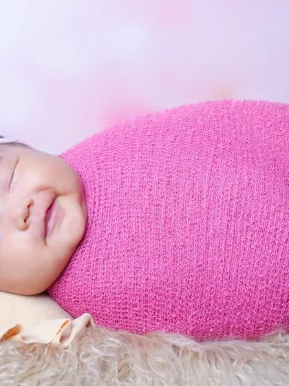 A beautiful smiling baby girl, happily swaddled in a bright pink wrap. It's a joy to capture these happy expressions when babies are awake and content.