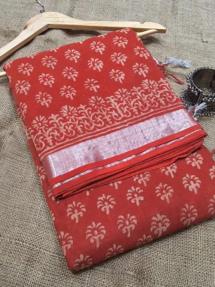 A perfect summer saree in red cotton linen with a simple handblock print and a silver zari border. It's lightweight, breathable, and comes with a matching printed blouse fabric.