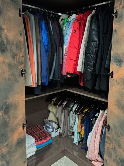 A corner closet organized to maximize storage, with hanging space for jackets and folded clothes below.