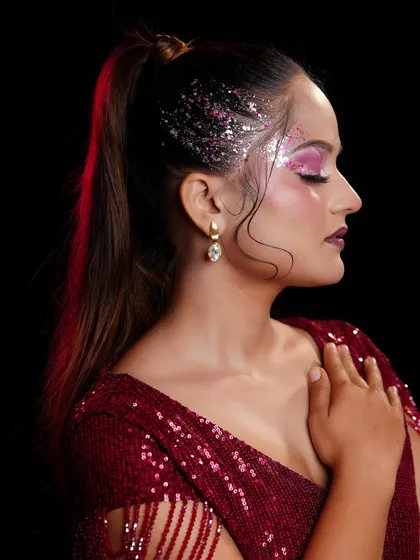 A side profile of a glamorous party look, highlighting the pink glitter eyeshadow and sleek high ponytail.