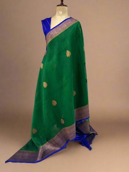 A rich bottle green pure Kora organza saree with gold butis and a contrasting royal blue border.