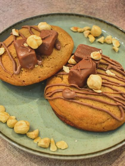 A Snickers lover's dream! These soft cookies are loaded with chocolate chunks, drizzled with nut butter, and topped with pieces of Snickers and roasted nuts for a full-on flavor party.