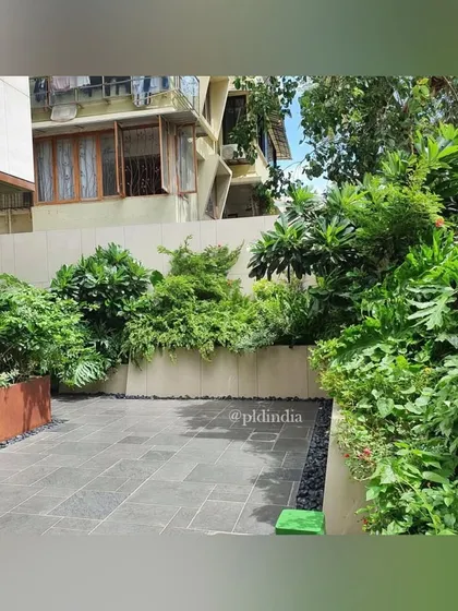 A paved courtyard is bordered by raised planters filled with a dense mix of shrubs and trees. This creates a green edge that defines the space and provides a pleasant view from the surrounding buildings.
