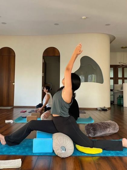 A student uses blocks and a bolster to support her in a deep split variation, demonstrating how props can make advanced postures more accessible and beneficial.