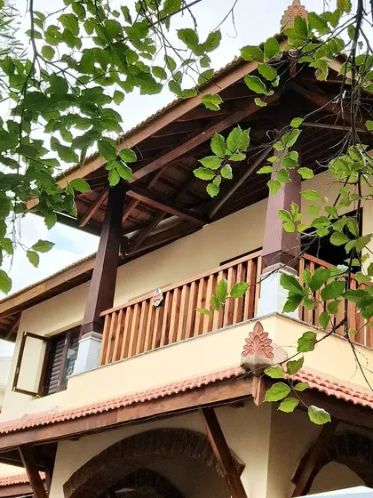 The west-facing balcony of the Basavanagudi house, featuring Indian mahogany railings and a wooden truss canopy. This space is designed to soften the harsh afternoon sun while allowing for pleasant breezes and views of the street.