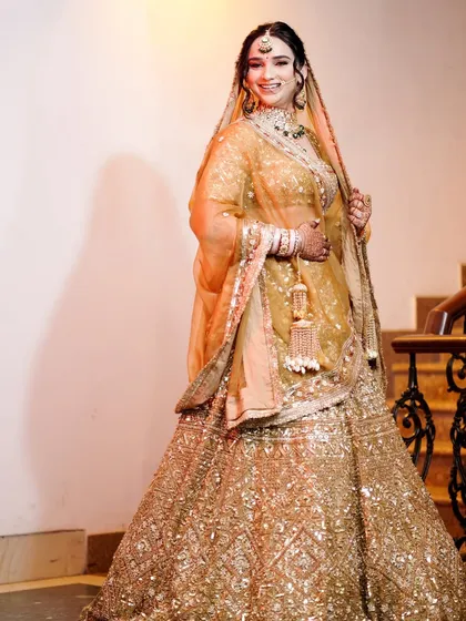 A full-length bridal portrait on a staircase, showcasing her golden lehenga.