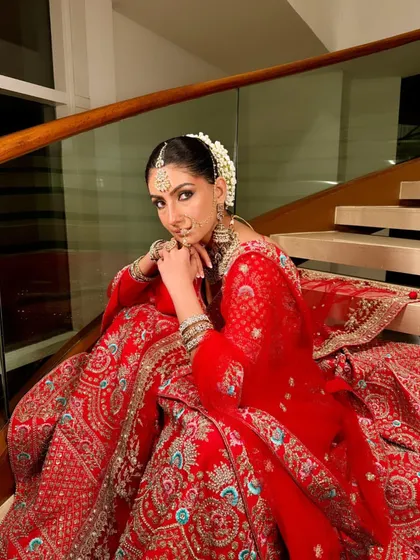 A regal portrait of a bride on a staircase. The red lehenga and classic makeup create a powerful and timeless image of bridal beauty.