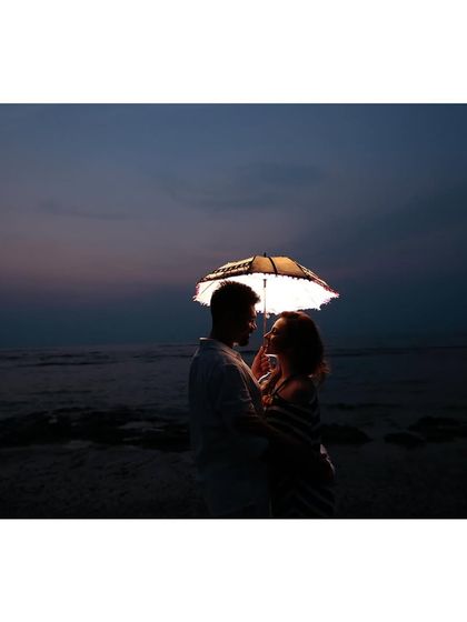 A creative and romantic shot using a lit umbrella to illuminate the couple against the night sea. This technique adds a magical and unique element to pre-wedding photography.