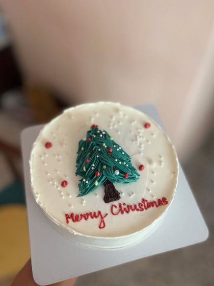 A simple and cute Christmas-themed cake. The design features a piped buttercream Christmas tree on a snowy white background.