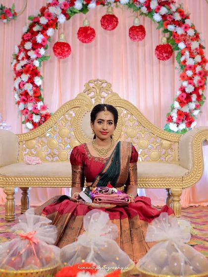 A full portrait of the bride seated on the stage, surrounded by traditional gifts and decorations for her engagement ceremony.