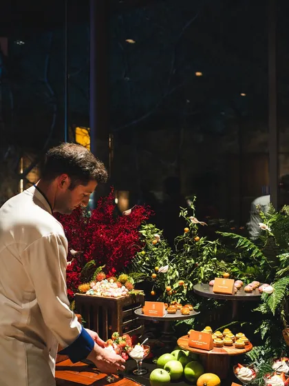 Another view of Chef Maxime arranging the vibrant grazing table. The reflection in the glass behind him shows the seamless integration of our indoor and outdoor spaces.