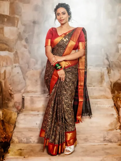 A full-length portrait showcasing a beautiful black and red silk saree. The bride stands on stone steps, creating a classic and elegant composition.