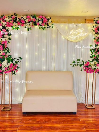A lovely Roka ceremony setup in a banquet hall. The rectangular floral frame in pink and white, paired with a 'Better Together' sign and a comfortable sofa, creates a perfect stage for the couple.