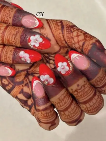 For the bride who loves red. This set features a mix of bold red nails and French tips, all adorned with 3D flowers and pearl centers to match the henna design.