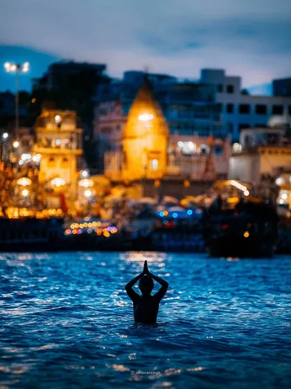 This is the same powerful moment of devotion in Varanasi, captured from a slightly different angle. The deep blue of the water contrasts with the warm, illuminated city, creating a spiritually charged image.