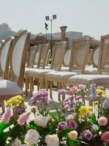 The elegant guest seating arranged for the ceremony. The clean lines of the chairs contrast beautifully with the organic, lush floral arrangements lining the aisle.