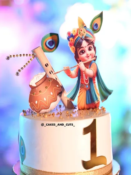 A close-up of a Krishna-themed cake for a first birthday. The detailed topper shows little Krishna playing his flute, perfect for a "Kanha" theme party.