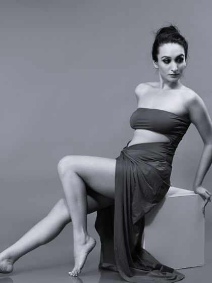 An elegant, full-body monochrome portrait. The model's pose is reminiscent of a classical sculpture, highlighting grace and form.