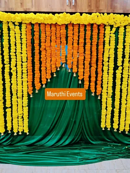 A classic and always beautiful backdrop made of dense yellow and orange marigold garlands. This traditional setup is perfect for Mehandi ceremonies, pujas, or any festive occasion, set against a rich green velvet drape.
