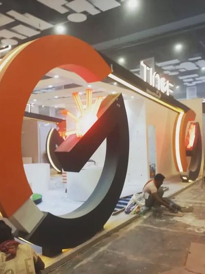 The Tinge booth under construction, with its large, striking orange circular elements taking shape.