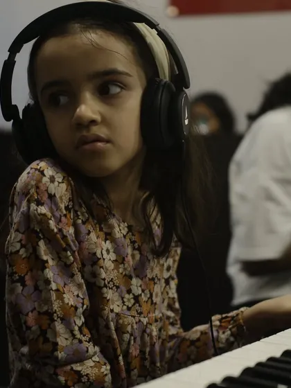 A young student wearing headphones, listening intently during her piano lesson. Aural training is a key component of our curriculum.