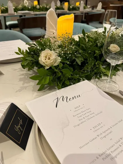 A detailed shot of the green and white tablescape, focusing on a custom place card and menu. A single white rose in the floral arrangement adds a touch of classic elegance to the birthday dinner decor.