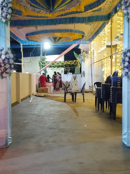 A glimpse of an outdoor wedding reception being set up under a large tent. The pillars are wrapped in light blue and white fabric with floral accents, and the ceiling is draped in blue and yellow cloth.