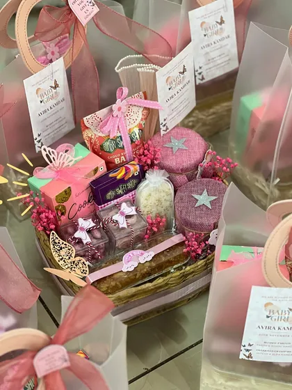 A fully assembled basket-style announcement hamper, overflowing with pink and purple treats and decorated with delicate butterflies.