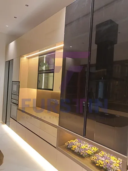 Here you can see the reflective, high-gloss sliding panels used to conceal storage areas, maintaining a sleek and minimalist look. The open niche with floral arrangements adds a personal, decorative touch.