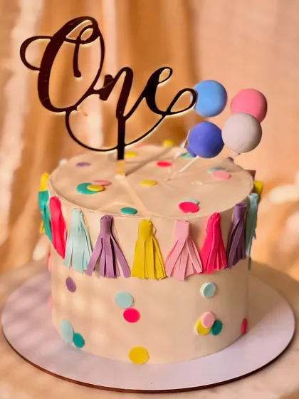 A festive and colorful cake for a first birthday party. This lemon-flavored cake is decorated with a fun tassel garland, confetti dots, and a balloon topper.
