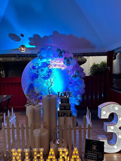 A mermaid-themed party with dramatic blue lighting. The setup includes a circular backdrop with a mermaid graphic, a neon sign, and a large marquee number '3'.