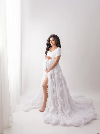 A full-length portrait by the window, capturing a classic and elegant pose. The simplicity of the white-on-white setup is timeless.