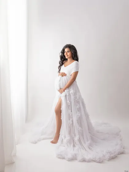 A full-length portrait by the window, capturing a classic and elegant pose. The simplicity of the white-on-white setup is timeless.