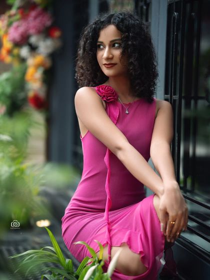 A beautiful portrait of a model in a vibrant pink dress, set against a backdrop of colorful flowers. This shot was taken outdoors, using a cafe's floral display to create a romantic and charming setting.