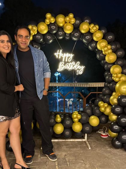 A couple posing in front of the stylish black and gold balloon arch with a neon sign on their terrace.