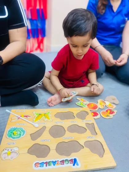 Learning happens everywhere, especially during focused play. A toddler works on a wooden vegetable puzzle, developing fine motor skills, problem-solving abilities, and early vocabulary. We provide a variety of age-appropriate educational toys to stimulate cognitive growth.
