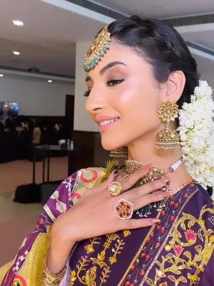 A side profile of the radiant bride, showcasing the intricate hairstyle with gajra and the flawless, glowing skin.