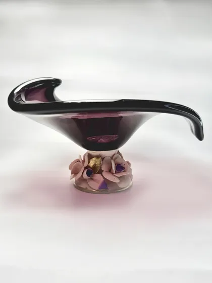 Handcrafted brilliance from Murano, now in your home. This deep amethyst glass bowl features a dramatic, sweeping form, resting on a base of delicate porcelain flowers, creating a stunning contrast.