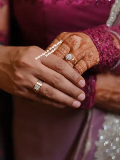 A tender moment between the engaged couple, their hands intertwined, showcasing both the bride's intricate mehendi and the groom's ring.