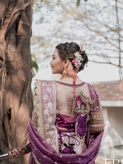 The back view of this stunning bridal look is just as important. Here you can see the detailed blouse work, the neat hairstyle with fresh flowers, and the elegant fall of the Nauvari's padar.