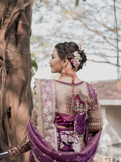 A detailed view of the bride's back, showcasing the unique blouse design and the beautifully arranged hairstyle with floral accents.